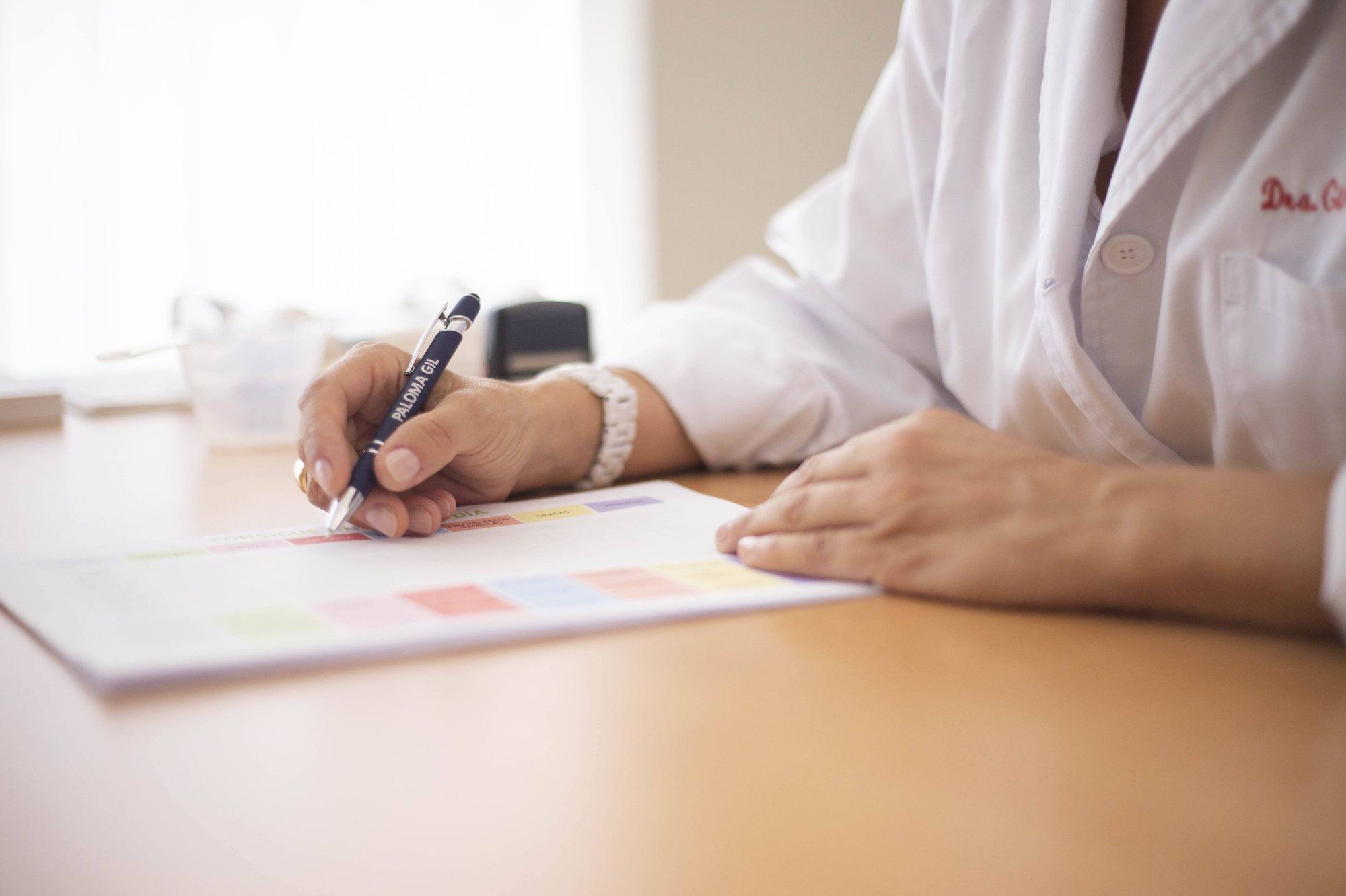 Médica de jaleco à mesa do consultório, registrando anotações do plano da paciente